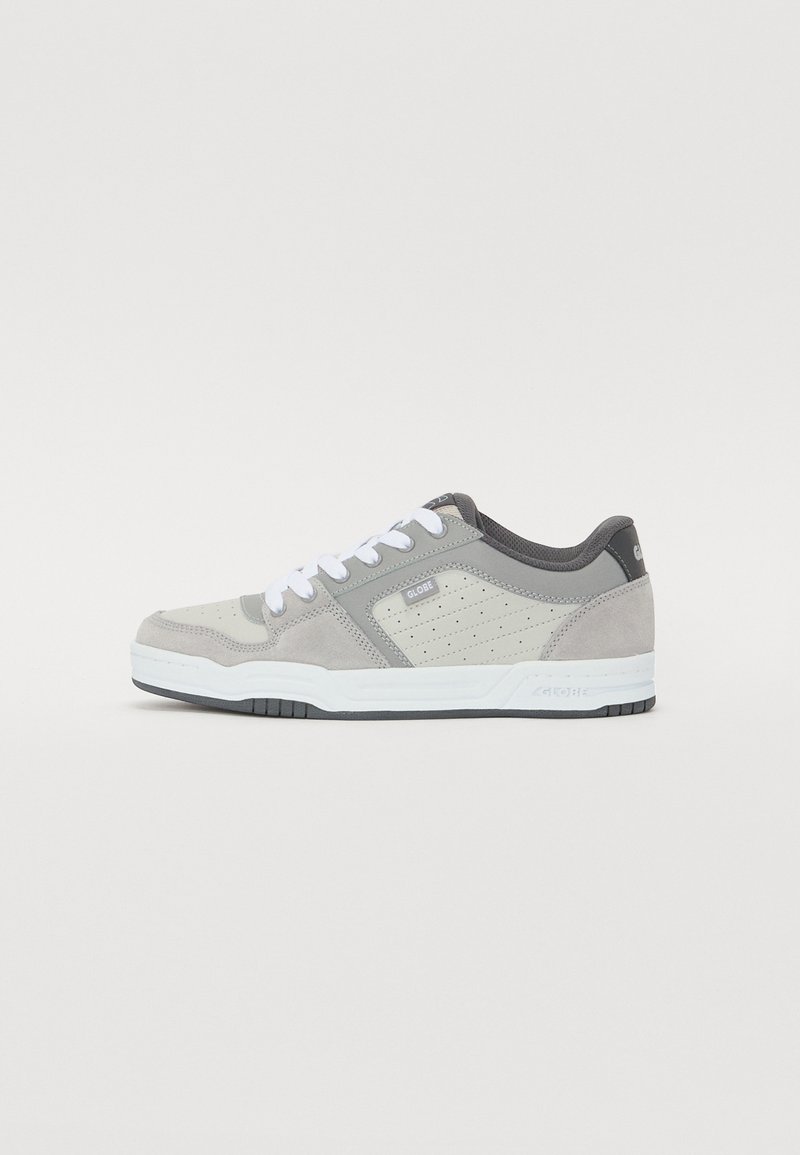 Helle Graue Sneaker mit einem perforierten Obermaterial, aus Wildleder und Mesh-Materialien, weißen Schnürsenkeln und einer schwarzen Gummisohle. Mit "GLOBE"-Logo.