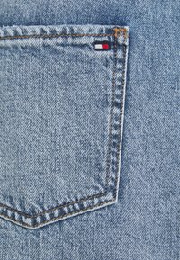 Takapocketi denim sinihousut, jossa on punainen, valkoinen ja sininen logo-painatus, oranssi ommeltu yksityiskohta ja teksturoitu kangas.