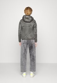 Šedá prošívaná bunda s kapucí, která má prošívaný design a lesklou texturu, v kombinaci s šedými džíny s vysokým pasem a bílými teniskami.