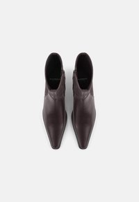 Donkere bruine leren enkellaarsjes met een smalle, puntige neus en een gladde textuur, voorzien van een rits aan de zijkant en een minimalistisch ontwerp.