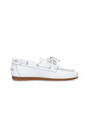 Witte geweven leren loafer met zijstrikdetail en bruine platte rubberen zool, getoond in profiel tegen een witte achtergrond.