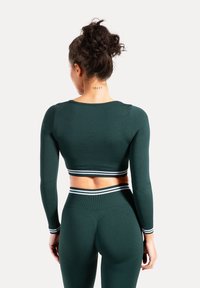 Groen, aansluitend crop top met lange mouwen en bijpassende legging met witte strepen bij de boorden en tailleband, gemaakt van rekbare, getextureerde stof.