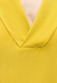 Tissu jaune texturé avec un décolleté en V profond et un détail froncé subtil au centre devant.