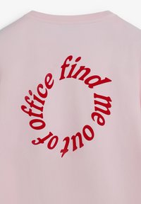 Camiseta rosa con un texto rojo en negrita que dice "encuéntrame fuera de la oficina" en un patrón circular en la parte posterior. Material de algodón suave.