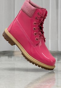 Botim de tornozelo rosa à prova d'água com um acabamento brilhante, colarinho texturizado rosa, sete ilhós e uma sola de borracha robusta e sulcada.