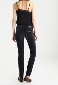 Svarta slim fit-jeans med en slät yta, med bakfickor och en utsmyckning på midjebandet. Matchas med en svart topp med spetsdetaljer.