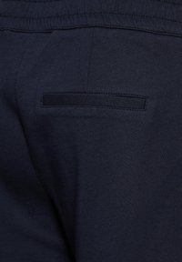 Nära bild av marinblå byxor med elastisk midja och en enkel insydd bakficka på högra sidan.