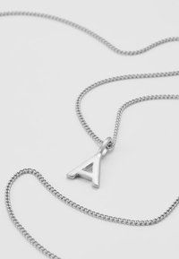 Collana in argento con un pendente a forma della lettera "A" in evidenza e con dettagli a intaglio. La catena ha un aspetto texturizzato con anelli intrecciati.