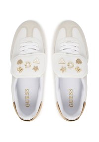 Zapatillas blancas y crema con cierre de cordones, acentos de ante y herrajes dorados decorativos que incluyen emblemas y formas en la correa.