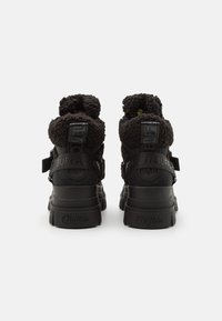 Black high-top shoes with fluffy shearling accents, a textured rubber sole, and a branded strap across the back for support and style.