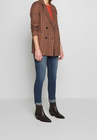 Brun rutig dubbelknäppt kavaj med långa ärmar, i kombination med mörkblå jeans och bruna ankelstövlar. En enkel, skräddarsydd design.