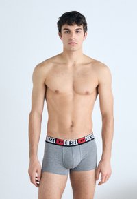 Boxer-briefs en coton gris avec une ceinture de marque noire et rouge. Le design présente une coupe ajustée et une texture lisse. Le modèle se tient droit.