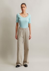 Lichtblauw getailleerd T-shirt met korte mouwen, gecombineerd met hoogzakelijke gestreepte beige broek met knoopdetails en een wijd uitlopende pasvorm.