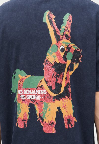 Ένα πολύχρωμο σχέδιο πινιάτα γαϊδουράκι με πράσινα μπαλώματα και λευκό κείμενο "Les Benjamins El Gringo" σε φόντο από σκούρο μπλε ύφασμα.