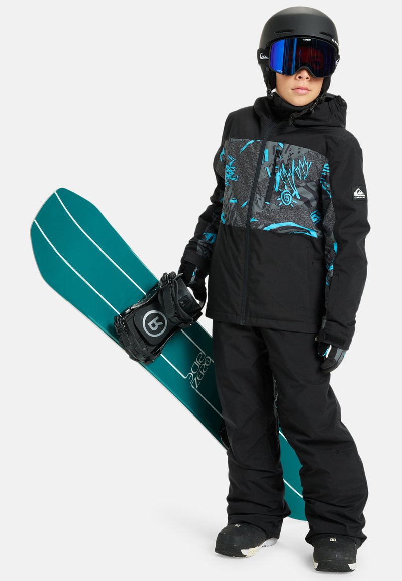 Čierna snehová bunda s tyrkysovými a sivými vzormi, čierne nohavice, rukavice a snowboard s tyrkysovými a bielymi pruhmi. Čierna prilba a okuliare.
