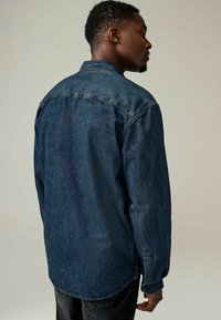 Jeans košulja u tamnoplavoj boji s opuštenim krojem, dugmadima na manžetama i klasičnim okovratnikom, s blagim efektom istrošenosti.