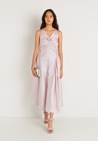 Φανάρι ροζ σατέν φόρεμα με εφαρμοστό κορσέ, πλισέ λεπτομέρειες και λουλουδένια αξεσουάρ στο κέντρο. Ροή, φούστα μήκους μέχρι τον αστράγαλο και σανδάλια με λουράκια.