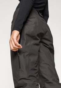 Μαύρο παντελόνι από ύφασμα με ημι-εφαρμοστό σχέδιο, διαθέτοντας τσέπη με φερμουάρ στο πλάι και λεία υφή, τονίζοντας λειτουργικές και σύγχρονες λεπτομέρειες.