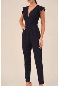 Marinblå jumpsuit med djup V-ringning, volangaxlar och avsmalnande ben. Tillverkad av ett mjukt tyg, med veck i midjan för form.