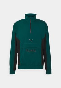Chaqueta de polo verde con cuello con cremallera, paneles laterales negros, con el logo y texto de PUMA en negro, fabricada con un tejido suave y texturizado.