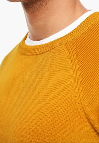 Senfgelbes gestricktes Sweatshirt mit Rundhalsausschnitt, geripptem Kragen und strukturiertem Muster. Verfügt über Raglanärmel und ein glattes weißes Innenfutter.