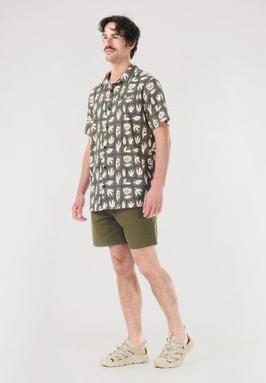Short-sleeve black shirt with white floral patterns, paired with olive green shorts. The outfit is completed with light-colored, rugged footwear.