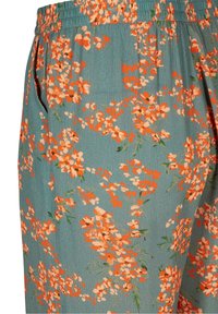 Blommigt mönstrade byxor i teal-tyg med orange och vita blommor, elastisk midja och sidofickor. Mjuk textur och lätt design.