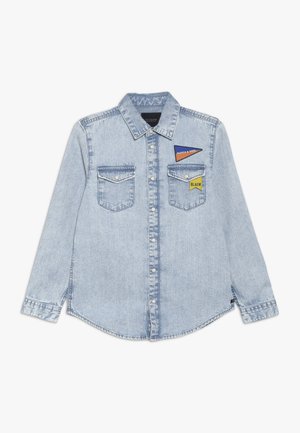 Jasnoniebieska koszula z długim rękawem z denimu, z zatrzaskami, dwie kieszenie na piersiach i dwie małe trójkątne naszywki na górnej lewej piersi.