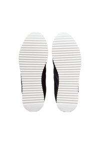 Zapatilla negra con parte superior de tejido texturizado, suela de goma blanca con surcos horizontales y logo visible en el lateral.