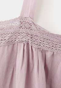Vêtement sans manches lilas avec une large bretelle ornée d'une bordure en dentelle florale décorative et un tissu doux froncé sous la bande en dentelle.