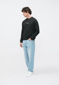 Felpa nera a maniche lunghe con scollo rotondo e scritta bianca, abbinata a jeans azzurri larghi e sneakers bianche. Design semplice, look casual.