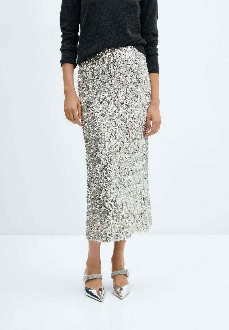 Haut noir à manches longues assorti à une jupe midi argentée à sequins et à des talons argentés brillants pointus avec des brides cheville.