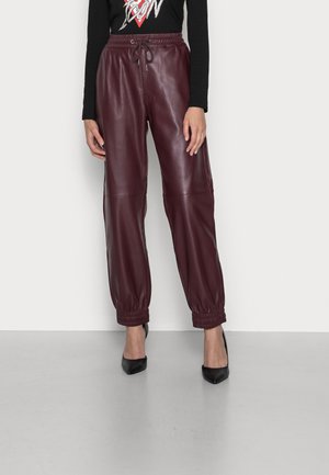 Woman wearing high-waisted burgundy leather jogger pants with elastic cuffs, paired with black pointed-toe heels and a long-sleeve black top.