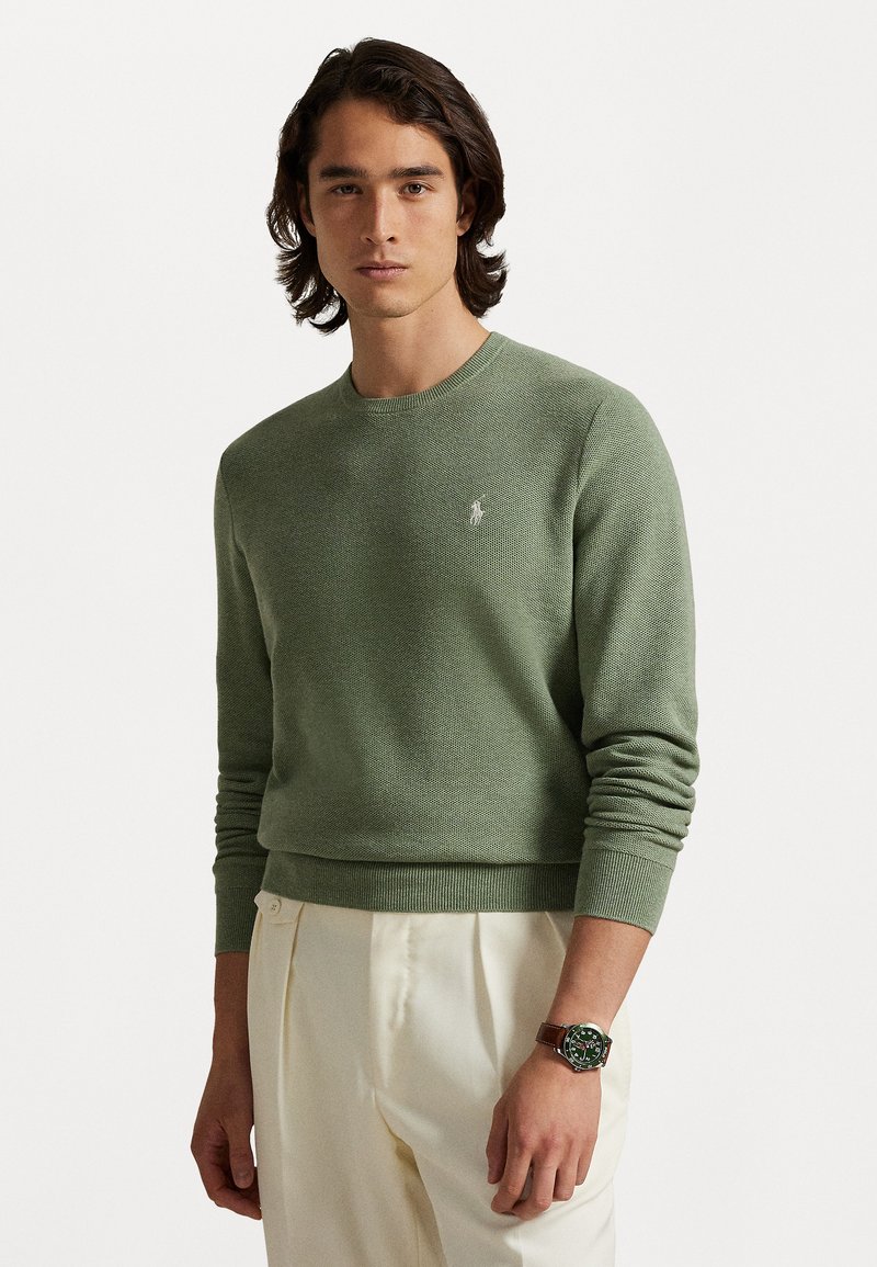 Hellgrüner gestrickter Pullover mit Rundhalsausschnitt und gerippten Bündchen. Verfügt über ein kleines Logo auf der Brust. Kombiniert mit cremefarbenen Hosen.