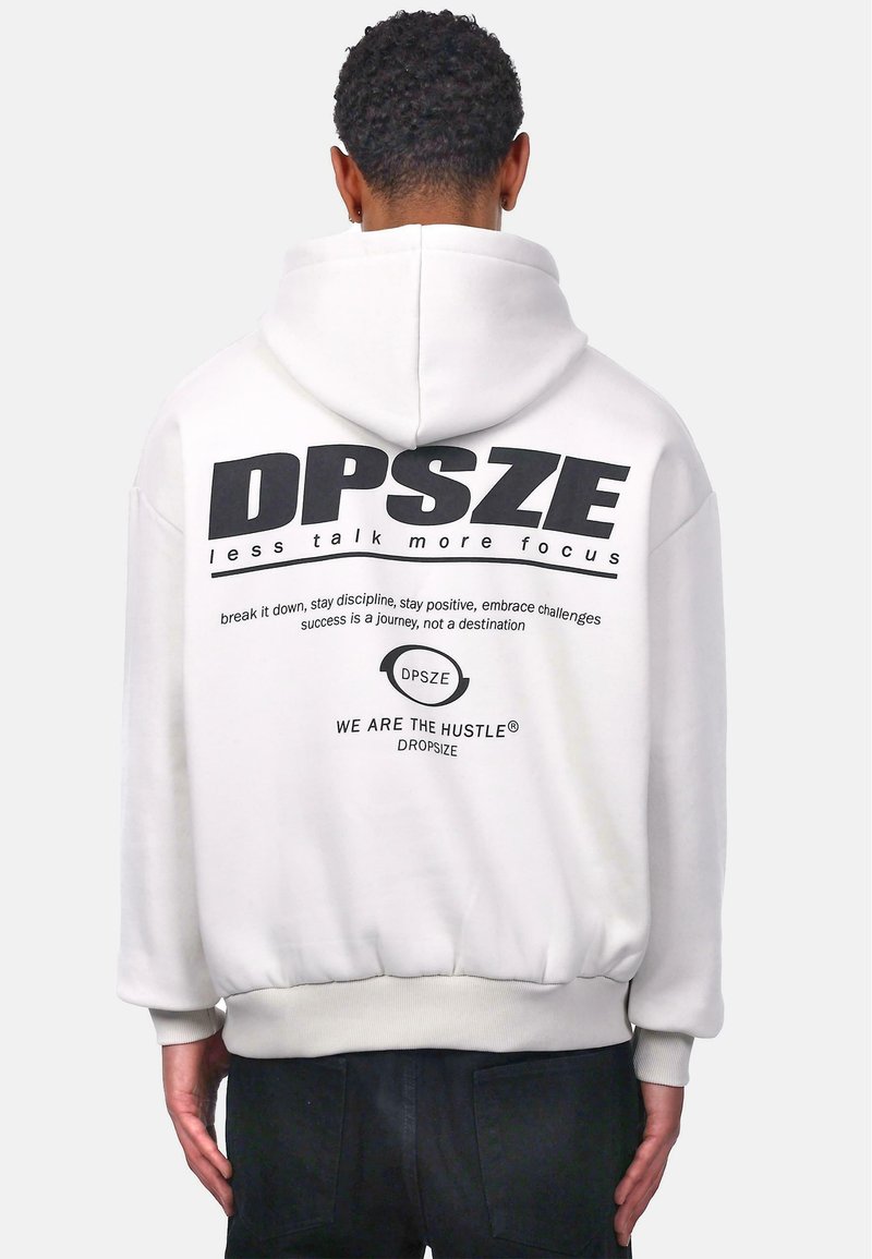 Sweat à capuche blanc avec un grand imprimé noir au dos, comprenant du texte et un logo. Manches et taille ajustées, texture de tissu douce.