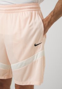 Lyserøde atletisk shorts med mesh-struktur, der har et sort swoosh-logo og en hvid skråstribe på den nederste del.