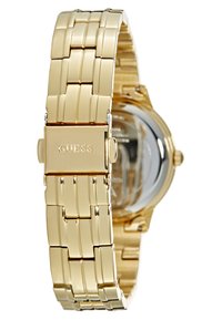 Gold metal watch with a linked bracelet design, featuring a clasp engraved with "GUESS." Transparent caseback showing internal mechanism.