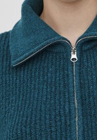 Sweatshirt zippé teal avec une texture côtelée et un large col. Doté d'une fermeture éclair argentée et d'une vue rapprochée des détails du tissu.