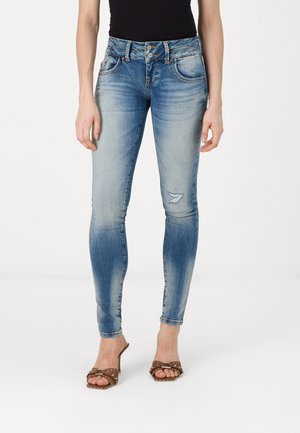 Tynne blå denimjeans med en falmet vask, to frontlommer og et lite hull. Stylet med brune sandaler med en dekorativ spenne.