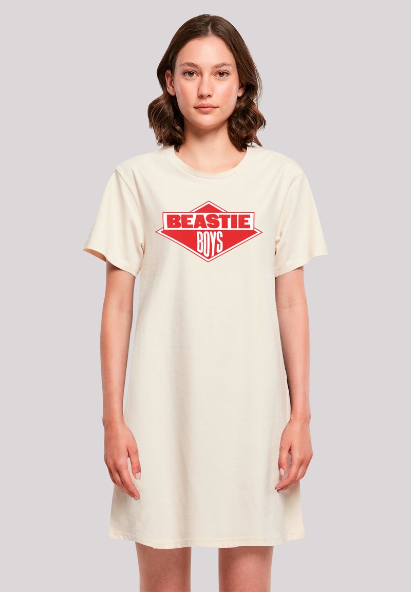 Beiges Baumwoll-T-Shirt-Kleid mit lockerem Schnitt. Auf der Vorderseite prangt eine kräftige rote Grafik in Rautenform mit der Aufschrift "BEASTIE BOYS".