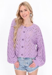 Cardigan tricotat lavandă cu un model de frunze, guler rotund și butoane mari. Prezintă mâneci tip balon și un design scurt, purtat peste pantaloni scurți din denim.