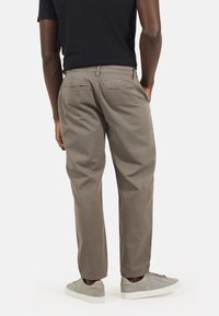 Pantaloni in cotone beige con una vestibilità rilassata, dotati di tasche posteriori e gamba leggermente affusolata. Abbinati a sneakers grigie chiare.