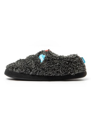 Zapatilla suave, gris oscuro y peluda con suela negra y etiqueta de marca azul en el lateral, diseñada para la comodidad y el calor en interiores.