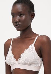 Lace bralette in soft pink with floral pattern, sheer cups, and a wide elastic band. Adjustable straps for fit and comfort.