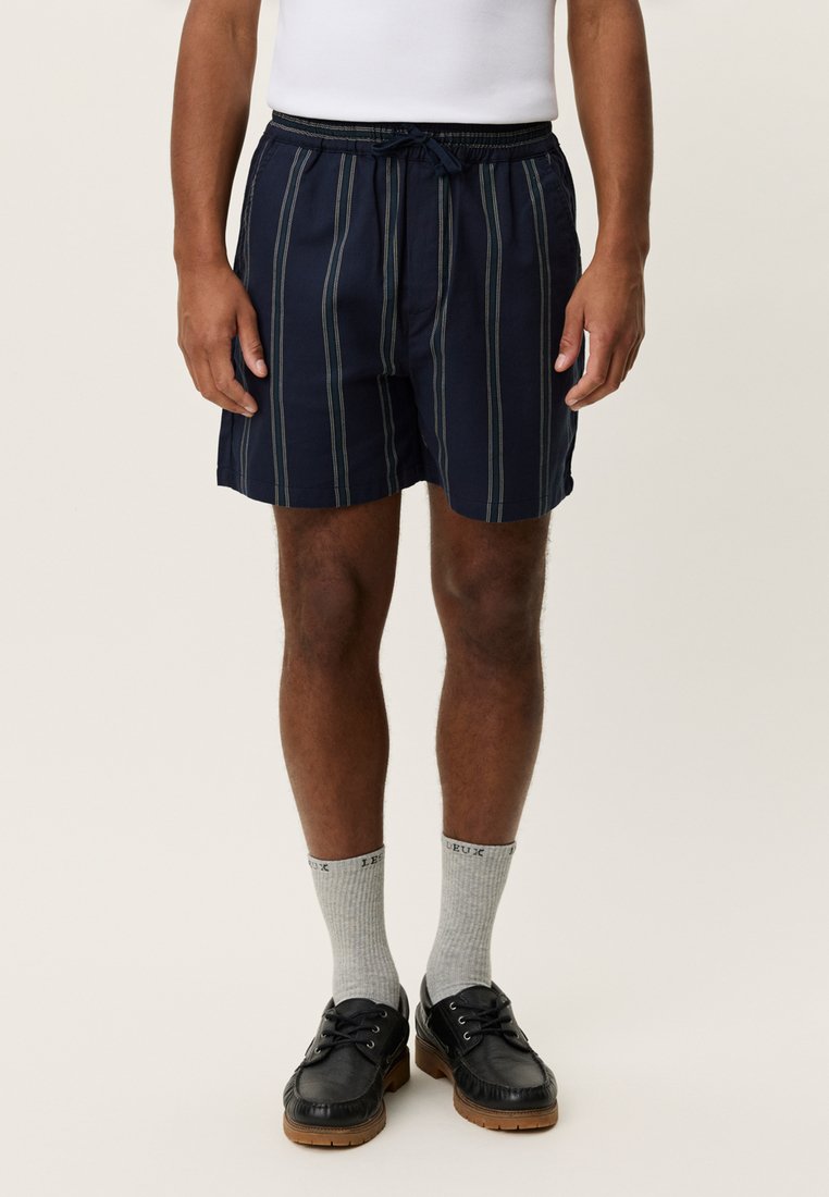 Shorts de bain à rayures bleu marine avec une ceinture élastique et un cordon de serrage. Tissu doux, longueur au-dessus du genou, associés à des chaussettes grises et des chaussures noires.