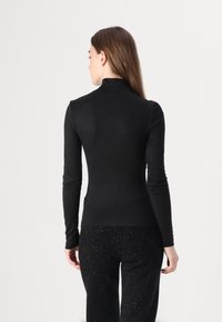 Haut à col roulé noir à manches longues, coupe ajustée, tissu doux, épaules sans couture et texture lisse, associé à un pantalon noir à motif tacheté.