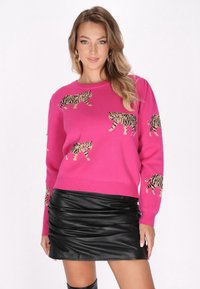 Fuchsia Pullover mit gestrickten Tiger-Mustern, rundem Ausschnitt und langen Ärmeln, kombiniert mit einem schwarzen Minirock aus Kunstleder.