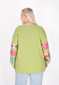 Maglietta verde a maniche lunghe con maniche decorate da motivi floreali, leopardati e geometrici. Tessuto morbido e vestibilità comoda.