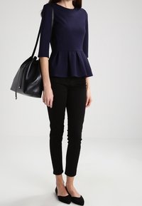 Námořnický peplum top s tříčtvrtečními rukávy, spárovaný s černými slim-fit kalhotami a černými balerínami. Černá kabelka dotváří celý outfit.