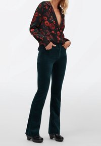 Zwarte bloemenblouse met diepe halslijn, gecombineerd met donkergroene corduroy flare broeken en zwarte klompen met zilveren studs.